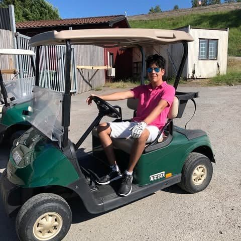 John sitter i en golfbil en solig sommardag