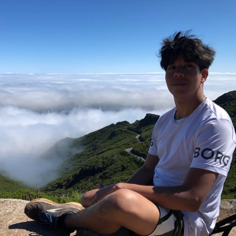 John sitter på ett berg ovanför molnen under en vandring