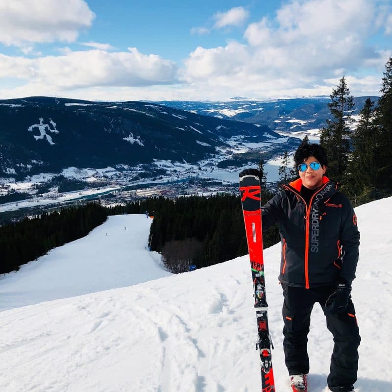 John står i en skidbacke med skidor i handen